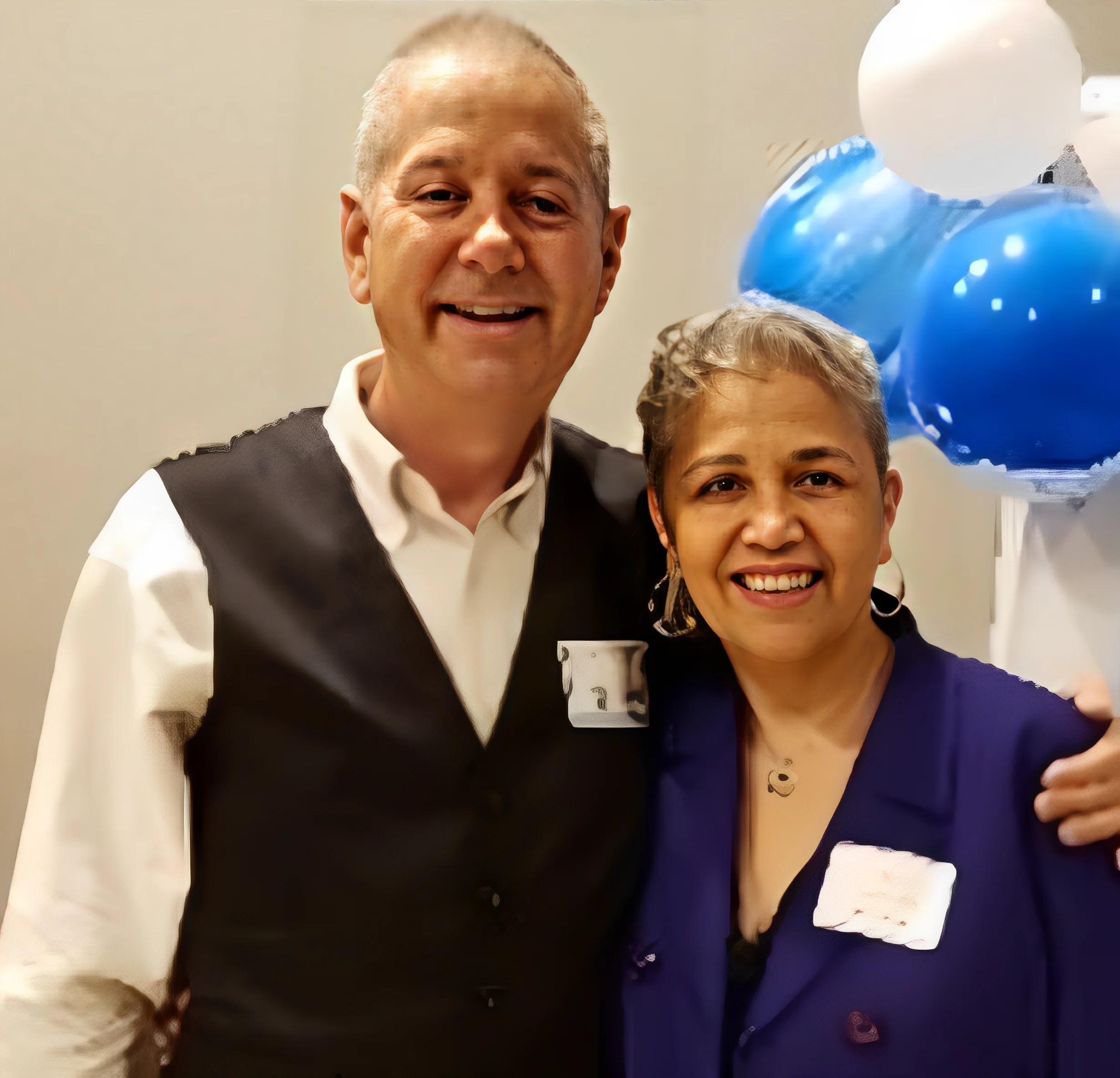 Smiling elderly couple posing with balloons in the background.