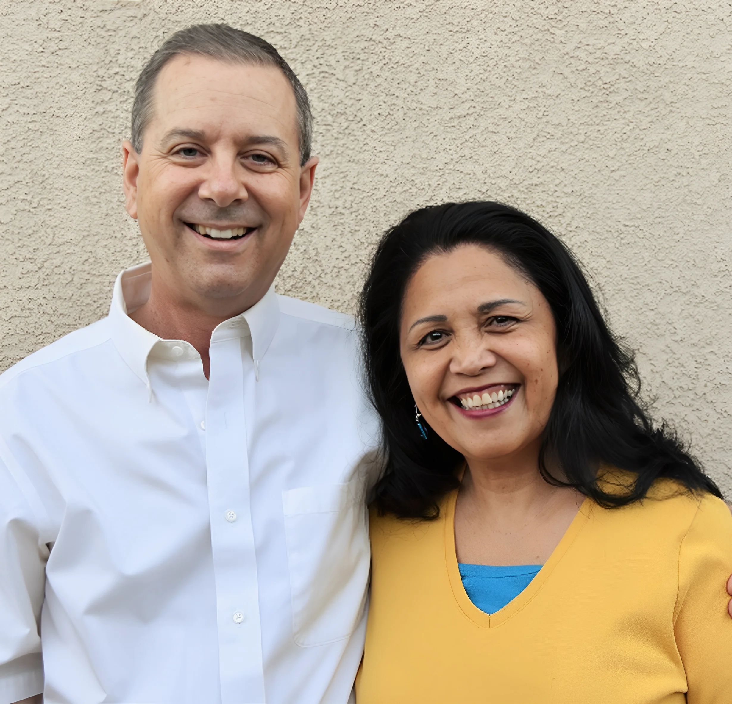 A smiling couple posing against a plain wall.