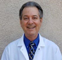 Smiling man in a white lab coat and tie.
