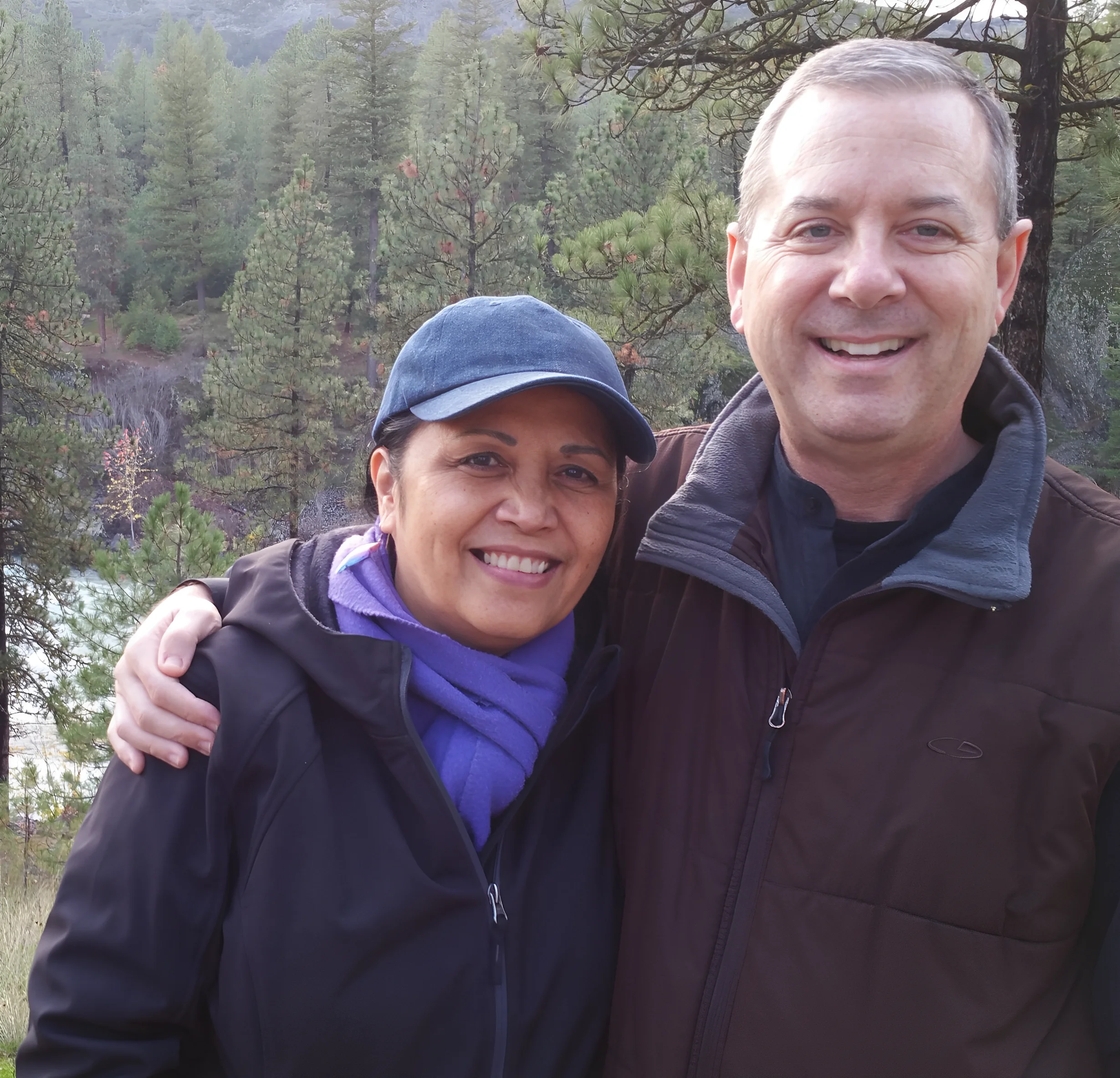 A smiling couple outdoors in a forested area.