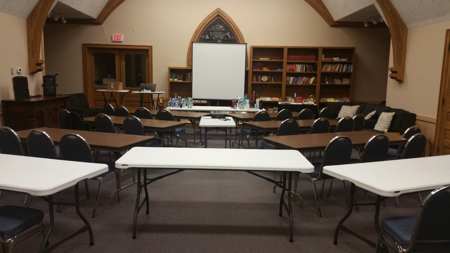 Empty meeting room with tables and chairs arranged facing a projector screen.