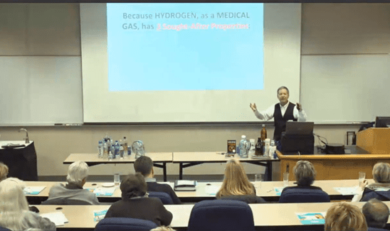Professor lecturing medical students in a classroom with a presentation slide.