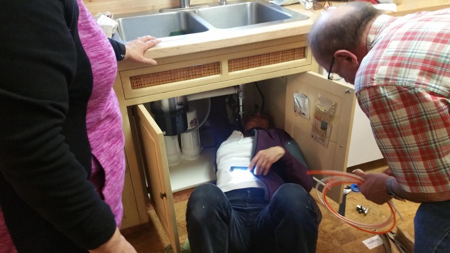 Person fixing plumbing under a kitchen sink.