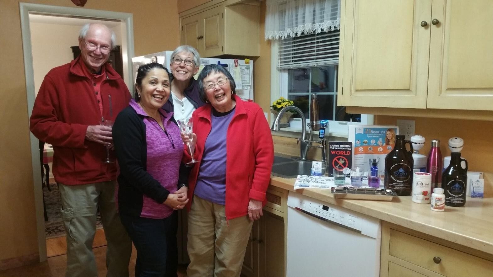 Four women smiling together in a cozy kitchen.