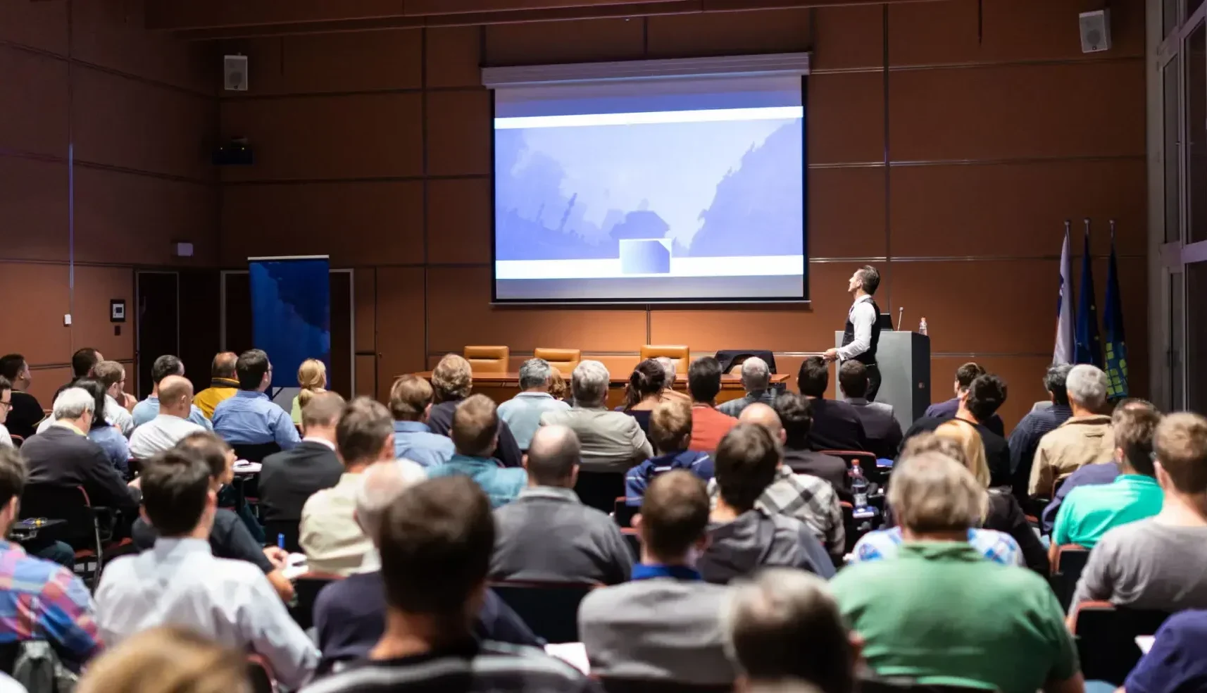 Audience watching a speaker with a presentation on screen.